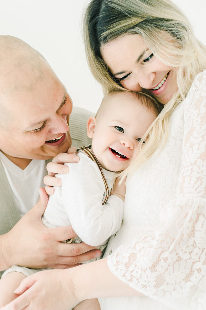 laughing baby snuggles between mom and dad