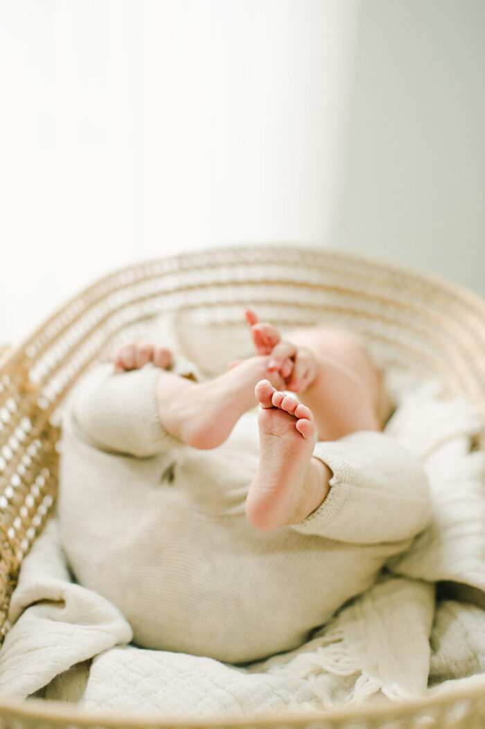 baby girl reaches for her toes in bassinet